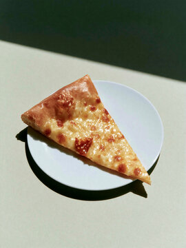 Cheese pizza slice on white plate in sunlight
