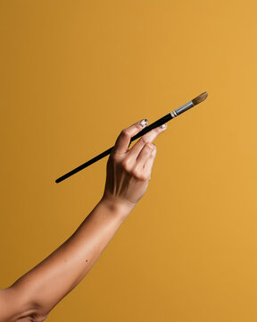 Painter's hand holding a paintbrush with paint-stained fingers on a yellow background