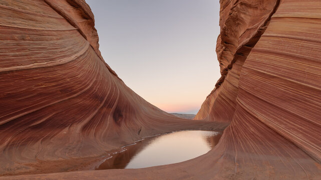 A still pool of water reflects the muted colors of the evening sky in a hollow between cliffs in the Wave formation in the Coyote Buttes Wilderness in Southern Utah, Northern Arizona USA. 