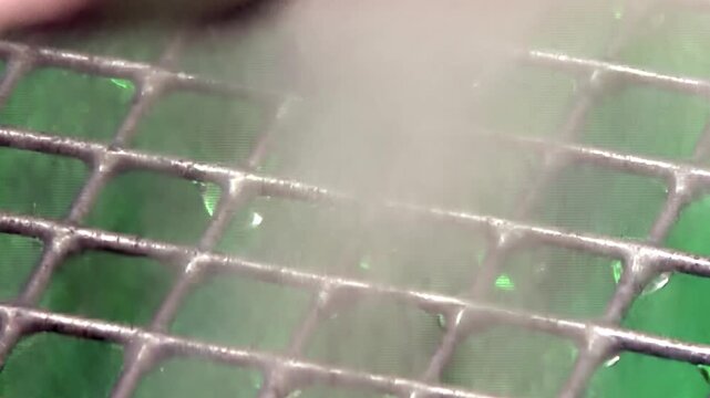 Delicate mist dances across a metal grid, showcasing a hydro filter in action. Tiny water droplets cling to the intricate lattice, actively scrubbing airborne impurities to deliver pure, crisp air.