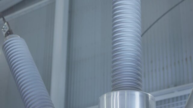Electricity equipment high voltage insulators suspended and slightly rotating inside industrial substation interior.