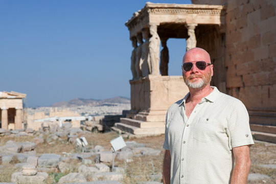 A traveler man stands before the Erechtheion on the Acropolis of Athens, Greece, admiring the Caryatids and the grandeur of ancient marble architecture.