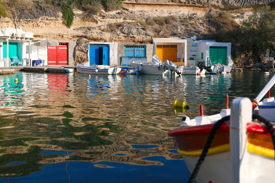 Brightly painted boathouses and small fishing boats line the calm waters of Mandrakia, Milos, Greece, reflecting vibrant colors across the Mediterranean harbor.