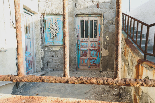 Faded turquoise doors framed by a rusted iron gate reveal the aged charm of Milos, Greece, where time and sea air shape the island&rsquo;s coastal architecture.