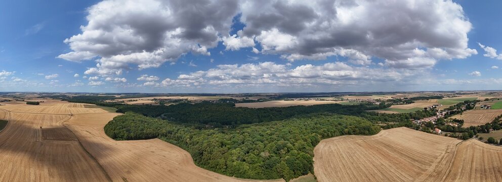 Vue a&eacute;rienne en Lorraine, les champs apr&egrave;s la moisson et au centre une for&ecirc;t. Les arbres sont verts , ciel bleu  nuageux avec des gros cumulus. La terre vue du ciel avec ses dessins artistiques nature