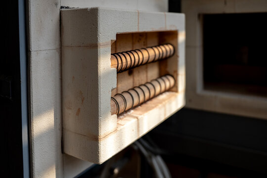 Heating coils and refractory firebrick inside open door of electric muffle furnace in ceramic art workshop, representing thermal processing equipment.
