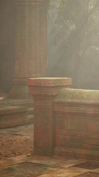 The scene shows ancient stone ruins surrounded by fog. Sunlight filters through trees, casting soft light on the weathered structures. The ground is damp and earthy, creating a moody atmosphere.