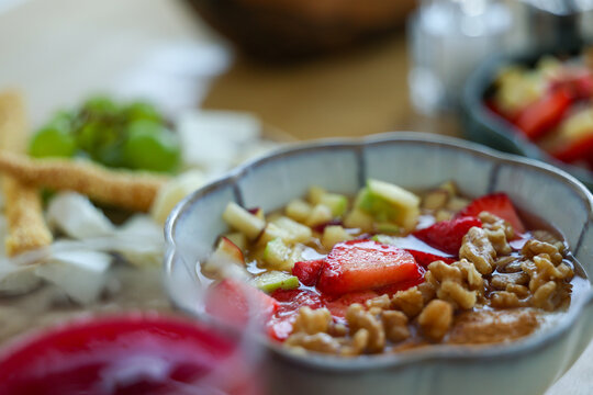 Breakfast oatmeal bowl topped with strawberries, walnuts, apple, and honey, served as a fresh and nutritious meal with natural ingredients.