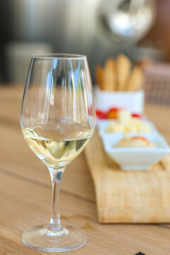 A glass of chilled white wine with cheese, fruit, and breadsticks on a wooden board in Greece, capturing Mediterranean sophistication and casual elegance.