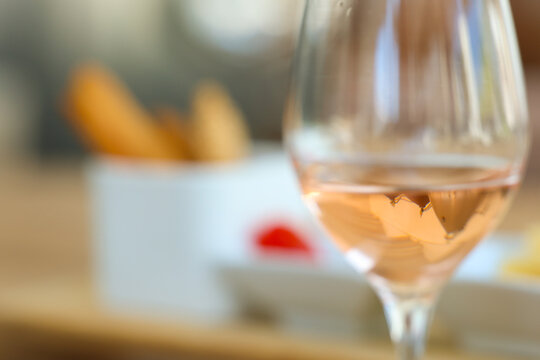 Glass of ros&eacute; wine with a softly blurred dining setting in the background, highlighting elegant hospitality, wine culture, and refined dining experiences.