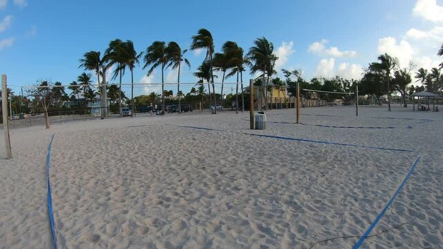 Vertical POV walk toward beach volleyball courts at Sombrero Beach in Florida at sunrise with golden light, palm trees and a tropical coastal atmosphere.