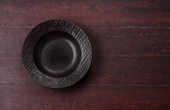An empty round ceramic plate on a dark, textured brown background. An empty round plate