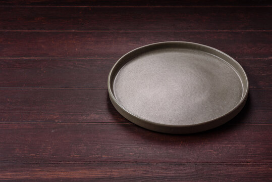 An empty round ceramic plate on a dark, textured brown background. An empty round plate