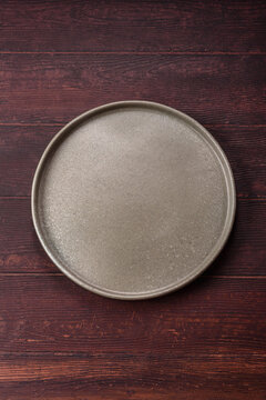An empty round ceramic plate on a dark, textured brown background. An empty round plate