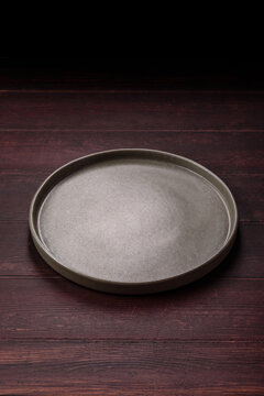An empty round ceramic plate on a dark, textured brown background. An empty round plate