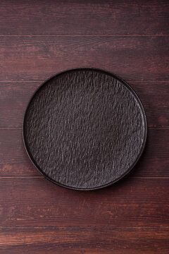 An empty round ceramic plate on a dark, textured brown background. An empty round plate