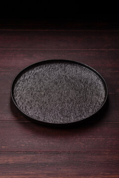 An empty round ceramic plate on a dark, textured brown background. An empty round plate