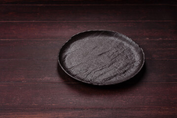 Obraz premium An empty round ceramic plate on a dark, textured brown background. An empty round plate