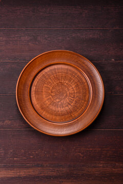 An empty round ceramic plate on a dark, textured brown background. An empty round plate