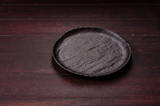 An empty round ceramic plate on a dark, textured brown background. An empty round plate