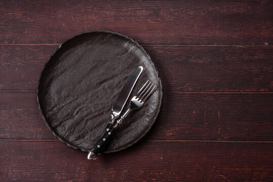 An empty round ceramic plate on a dark, textured brown background. An empty round plate