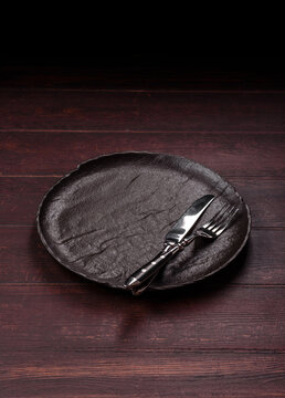 An empty round ceramic plate on a dark, textured brown background. An empty round plate