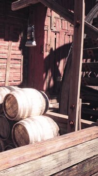Several wooden barrels are stacked next to a weathered building. The setting shows a mix of wood, shadows, and traditional elements. Light falls onto the barrels and surroundings.