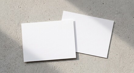 Fototapeta premium Top view of two blank white rectangular postcards on a light grey concrete background with soft shadows for stationery branding design.