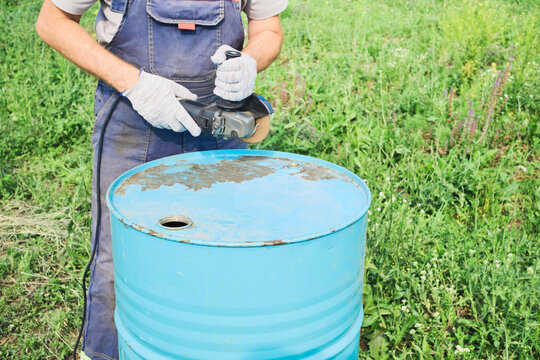 Worker holding angle grinder preparing to cut or grind metal barrel for diy project