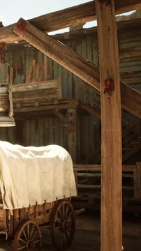 A wagon covered with a white cloth sits under a hanging lantern in a weathered area. The background shows wooden structures and stairs, indicating a rural location.