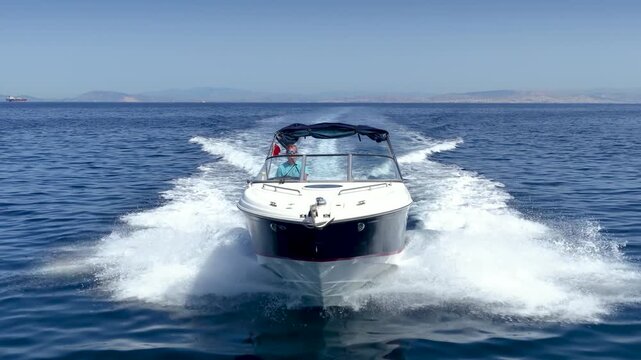 Aerial front view of a motorboat cruising with speed over the ocean and creating a trail of waves and surf