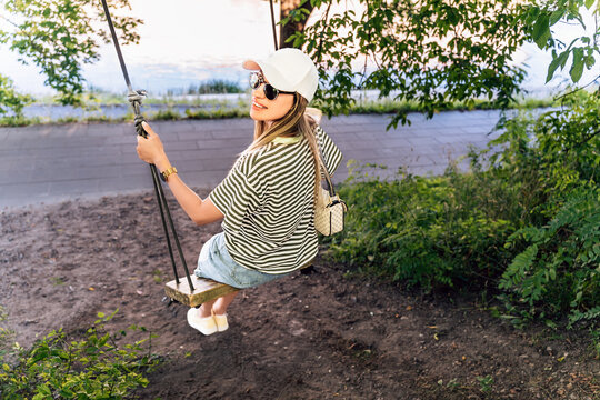 Woman on swing by riverside in summer city park