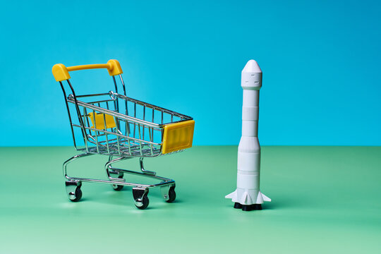 Shopping cart beside miniature rocket on colorful background