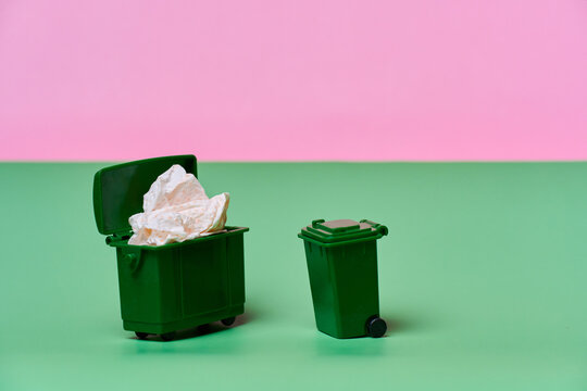 Overflowing trash bin beside empty wheeled garbage can