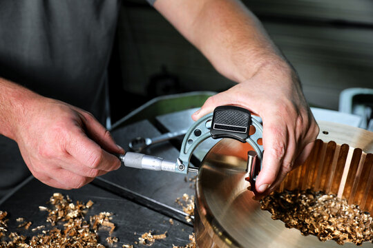 Technician measuring precision machined gear with micrometer in industrial workshop