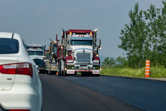 Quebec, Canada, 29 June 2026 : A convoy of Kenworth and Volvo semi-trucks drives on a paved road, seen from behind a passenger car.