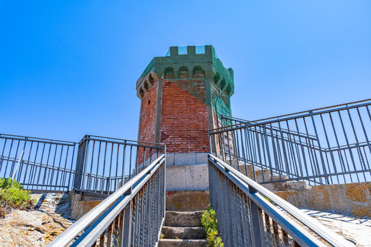Old brick tower in rio marina elba island with safety netting on top and metal railings for viewing platform