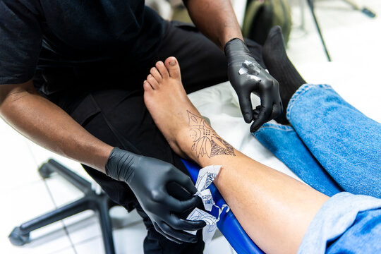 Tattoo artist applying stencil on client ankle in studio