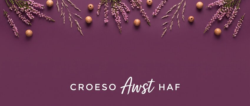Heather flower flat lay background with purple border, wooden beads, and Welsh language text Croeso Awst Haf for summer greeting header banner design with copy space for seasonal floral concept.
