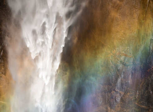 Misty Yosemite waterfall with rainbow spray on rock face