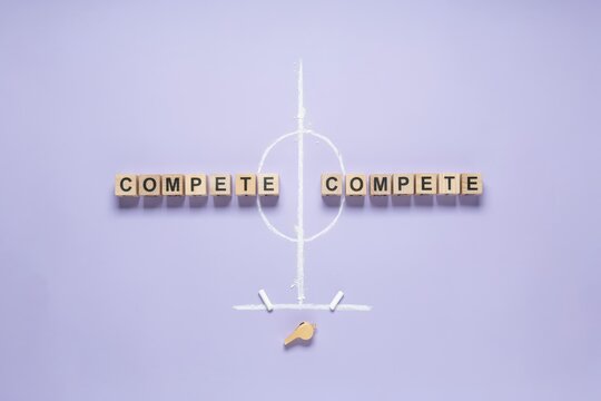 Wooden blocks spelling the word compete on both sides of a soccer field drawing on purple background