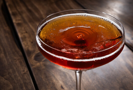 Closeup of a drop on top of a whiskey manhattan served on a rustic wooden background
