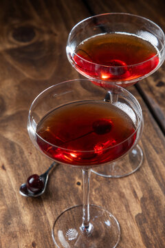 Two whiskey manhattans served with a cherry on a rustic wooden background