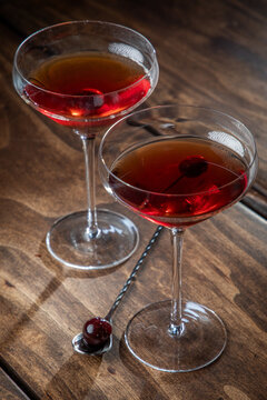 Two whiskey manhattans served with a cherry on a rustic wooden background