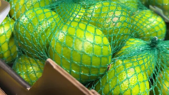 Green mesh bags filled with fresh limes create an attractive citrus display, offering convenient packaging for supermarkets, grocery stores and fresh produce markets. Close up.