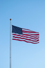 Obraz premium US American flag waving in the wind with beautiful blue sky in background. American flag on blue sky USA. Flag waving. Independence day. 4th of july. Vote