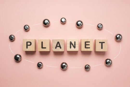 Wooden blocks spelling PLANET surrounded by metallic spheres in an orbit on a pastel pink background representing solar system concepts