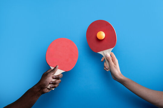 Multiethnic hands holding table tennis paddles on blue