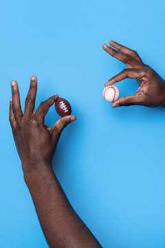 Hands holding football and baseball against blue background