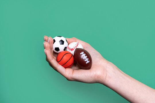 Hand holding miniature sports balls against green background